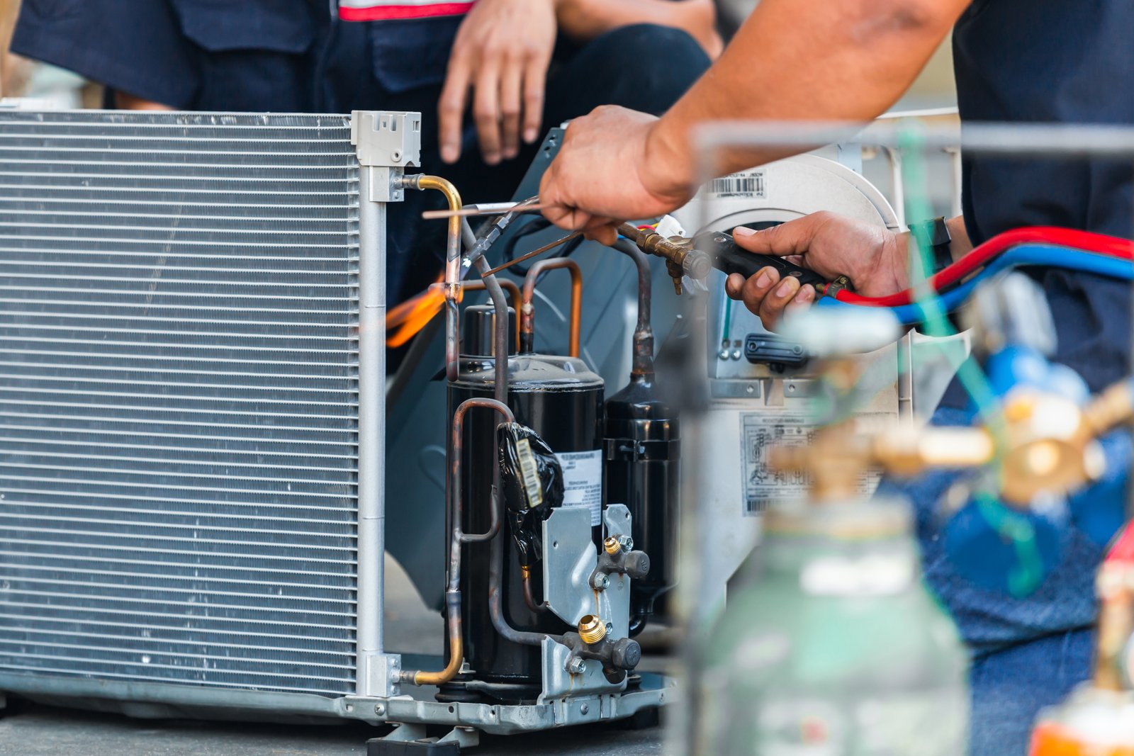 HVAC technician performing routine maintenance on an air conditioning compressor unit, using a torch to service copper refrigerant lines.