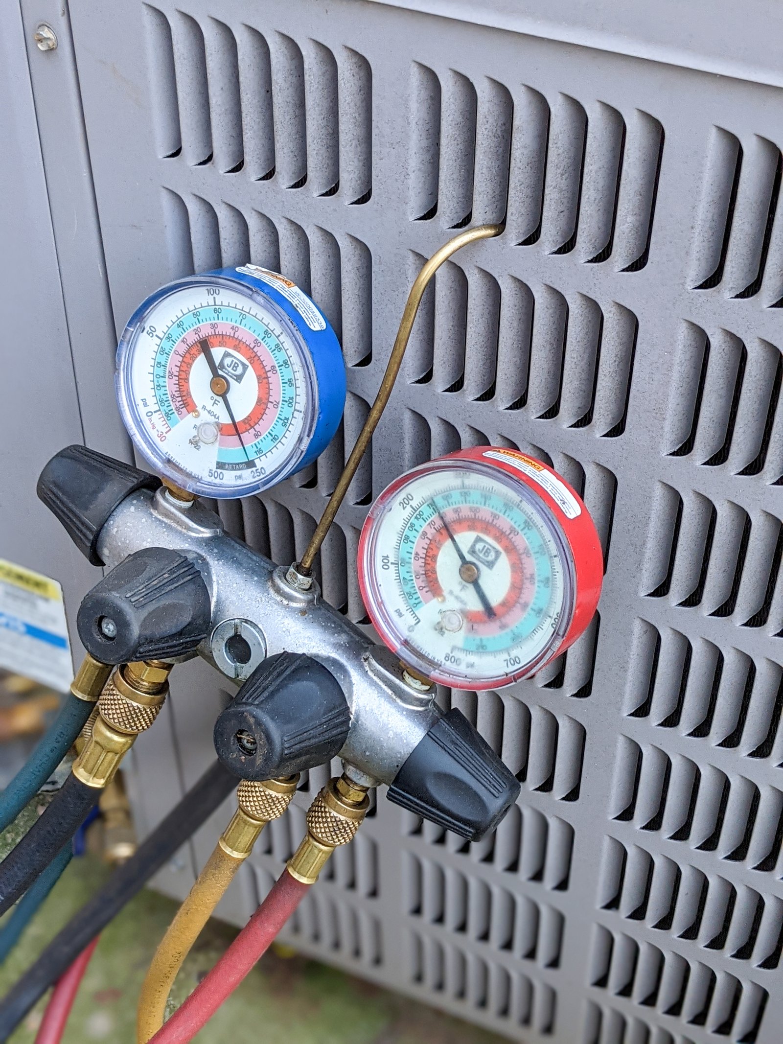 ac manifold gauge set connected to an outdoor air conditioning unit, measuring refrigerant pressure for system diagnostics and repair.
